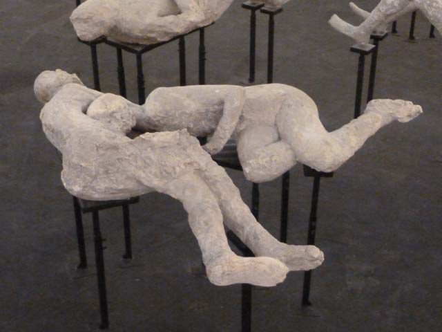 I.6.2 Pompeii. Victims 21 (rear) and 22 (front). 2015. Photo courtesy of Estelle Lazer.
According to Estelle Lazer, Cast Numbers 21 and 22 were embracing but, as they were cast separately, they could enter the gantry of the CT scanner individually. 
These two victims have variously been interpreted as two lovers or two women, sometimes as sisters or as a mother and daughter. 
The preliminary results of DNA analysis of skeletal samples from these casts indicate that they were two unrelated males.
Victim 21 has an age estimation of fourteen to sixteen years if the victim is a female, and fourteen to nineteen years if the victim is male.
Victim 22 must have been at least seventeen to eighteen years of age and the dentition suggested that this might be a younger adult as the surviving third molars had not erupted.
See Lazer E., et al. 2020. Inside the Casts of the Pompeian Victims: Results from the First Season of the Pompeii Cast Project In 2015. Papers of the British School at Rome.
