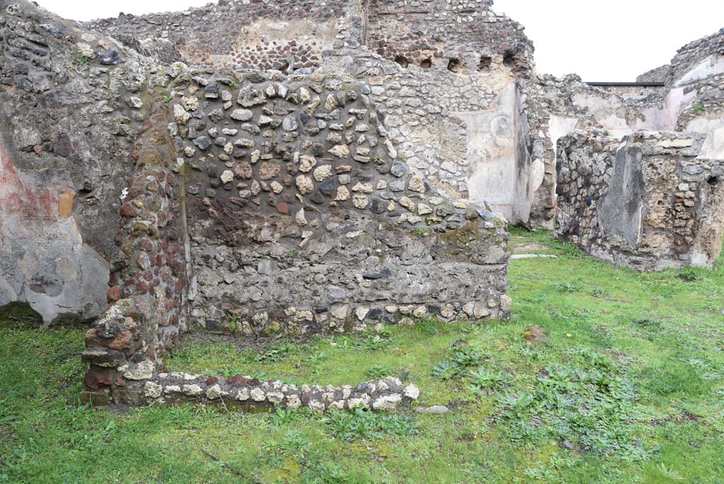 IX.5.18 Pompeii. March 2018.  Room “z”, looking north from atrium “b”, with room “g”, on left.
Foto Annette Haug, ERC Grant 681269 DÉCOR.
Zevi considered room “z” may have been a wooden lararium with a marble base.
See Zevi, F., 1964. La Casa Reg IX.5.18-21 a Pompei e le sue pitture: Studi Miscellanei 5. Roma: Bretschneider. (p.11, T: IX,1).
According to Sogliano, found in the second cubiculum on the left side of the peristyle, was the Genio Familiare.
See Sogliano, A., 1879. Le pitture murali campane scoverte negli anni 1867-79. Napoli: (p.10, no.11).
According to Boyce, on the east wall of the cubiculum was a lararium painting, the upper part had fallen. 
From a branch of the tree hung a head of a stag.
On the left of the tree, the figure of a small Genius is found, holding in his left, together with the usual cornucopia, a rudder which rested upon a green globe at his feet. 
To the left was a small altar, with the serpent gliding towards it. Further to left, was a huge tripod. 
On the right stood a male figure, nude except for a green cloak, in his left he held two long spears or poles.
See Boyce G. K., 1937. Corpus of the Lararia of Pompeii. Rome: MAAR 14. (p.86, no.427). 

