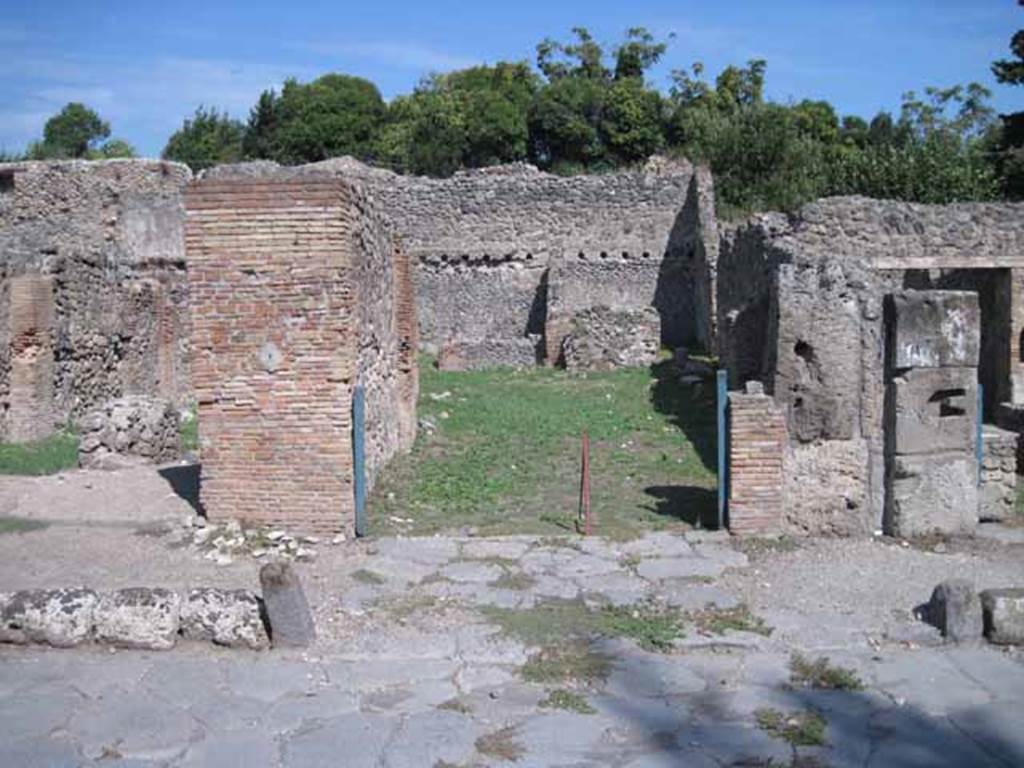 I.1.3 Pompeii. September 2010. Entrance, looking east across Via Stabiana.
Photo courtesy of Drew Baker.
According to Warscher, quoting Mau in Bull. Inst 1875, p.27,  “Per lasciar entrare i carri il marciapiede è interrotto avanti alla porta, e il selciato della strada continuato fino all’ingresso che è largo come quelli delle botteghe ed era chiuso mediante una porta a due partiti. La porta però non si fermava come al solito: nel bel mezzo della soglia di lava vi sono gli avanzi d’un uncino di ferro, e più a sinistra la buca per un chiavistello solo, mentre l’altro partito ne stava senza.  Invece al di fuori della porta si trovano nella soglia quattro buche quadrangolari, due vicine ai cardini, le altre m.0,20 discoste da quelle”.
See Warscher T., 1936. Codex Topographicus Pompeianus: Regio I.1, I.5. Rome: DAIR, whose copyright it remains (no.12).
(translation:“For the carts to enter, the pavement was interrupted in front of the doorway, and the paved roadway continued up to the entrance that was as wide as the doorway of the shops and was closed by means of a door with two entries. The door, however, didn't close as usual: in the middle of the lava threshold there were remains of an iron hook, and more to the left the hole for a latch only, whereas the other entry was without one. Instead outside the door in the threshold were four rectangular holes, two near to the hinges, the others 0,20m distant from those.")
