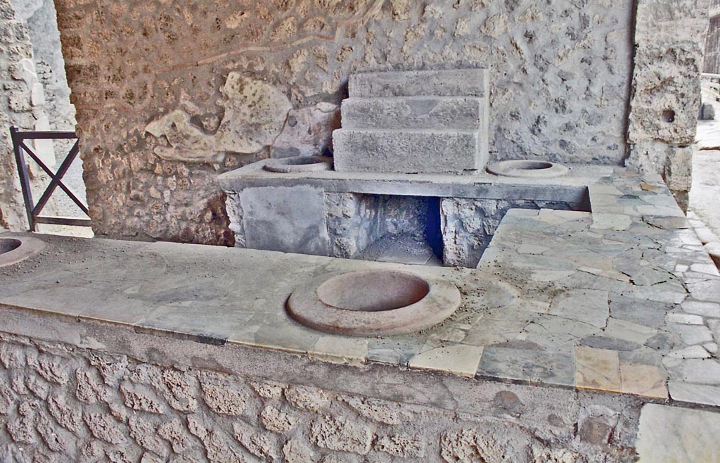 I.9.4 Pompeii. October 2001. Display shelving and two embedded dolia in counter against west wall. Photo courtesy of Peter Woods. 