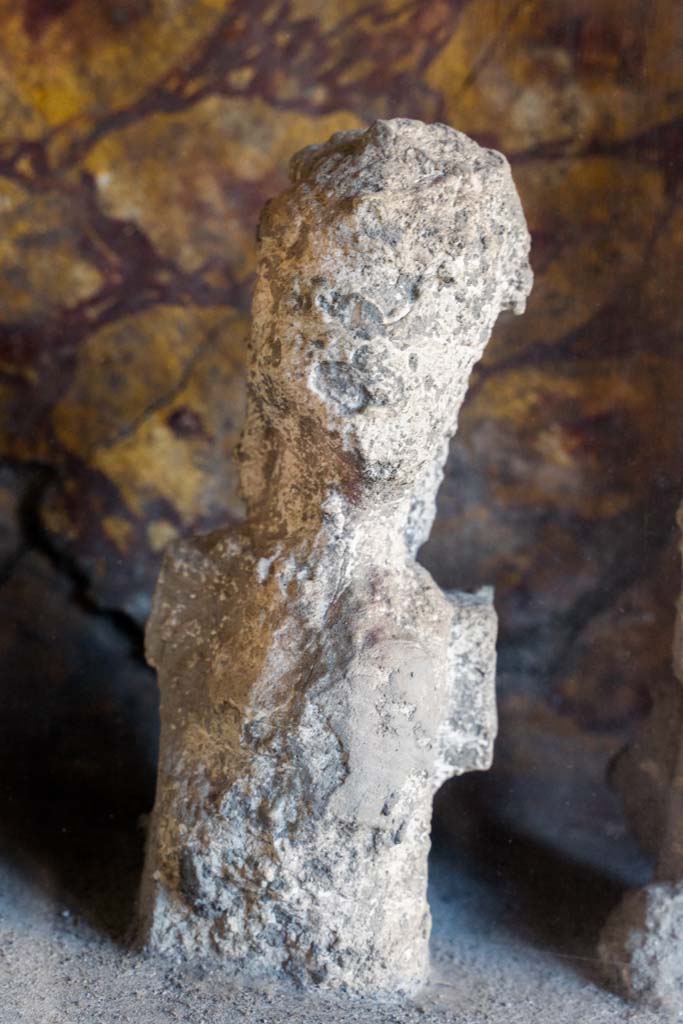 I.10.4 Pompeii. April 2022. 
Alcove 25, detail of plaster cast, seen on the right of centre, on the lararium or domestic shrine. (Image 1).
Photo courtesy of Johannes Eber.
