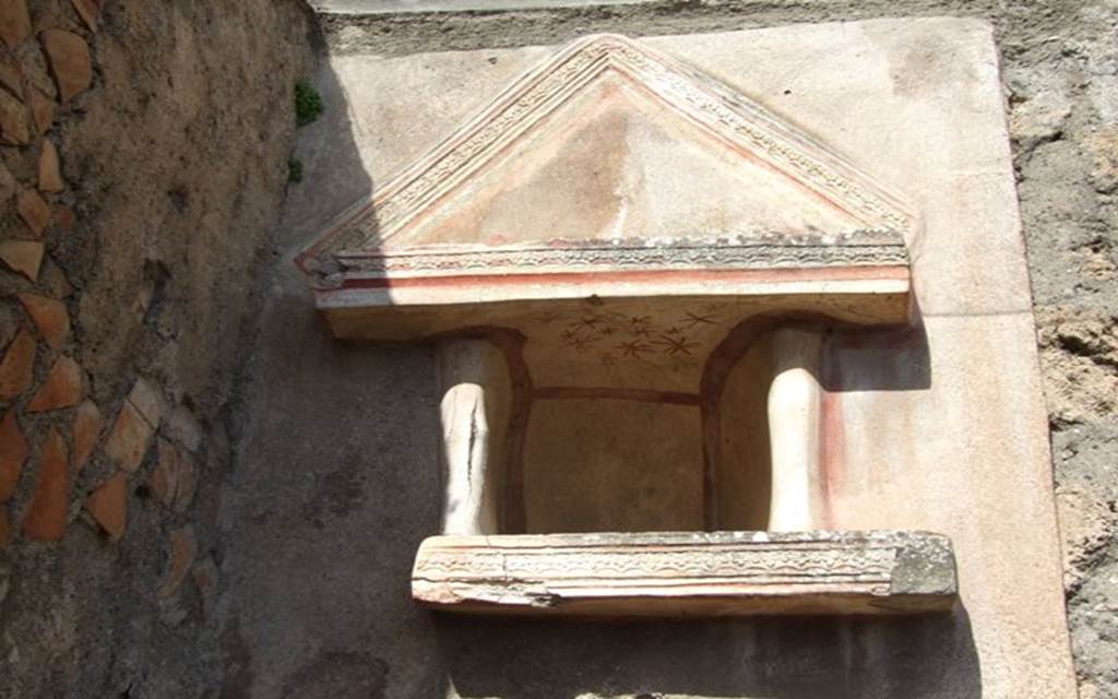 V.4.9 Pompeii. March 2009. Lararium niche. According to Boyce, this Lararium was on a special panel of rough white stucco, and was adorned with an aedicula faade. Beneath the niche was a heavy shelf with two columns resting on it, framing either side of the niche. The interior of the niche was white and outlined with red stripes. On the ceiling of the niche there were red and green star decorations. Within the niche were found the following figures  A bronze bust of Minerva, wearing the aegis and helmet. She was leaning backwards in a strange manner upon a bronze plate fitted with a sort of handle at the back.
A roughly worked alabaster figure of Venus wearing a crown, beside her to the left stands a small figure clad in a long garment. Venus seems to held her left hand around the smaller figure, while the latter placed her right hand upon the head of the goddess. This group stood upon a marble-covered base behind the bust of Minerva. A small standing male figure of ivory. Sogliano thought the figure was Venus, Mau thought it was definitely male.
Also found in the niche were two small rectangular terracotta altars and two terracotta plates. See Notizie degli Scavi di Antichit, 1899,pp.103. See Boyce G. K., 1937. Corpus of the Lararia of Pompeii. Rome: MAAR 14. (p.41, no.123, Pl.7,1).