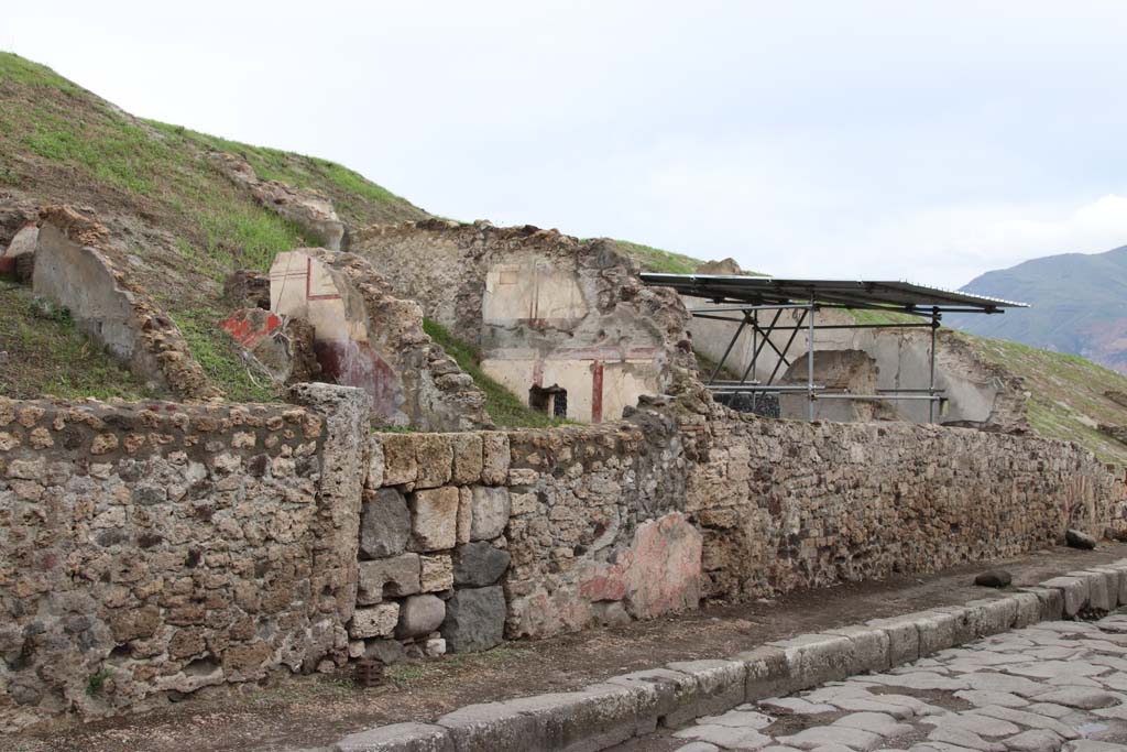 V.6.8 or 7 Pompeii, Pompeii. October 2020. Looking south along east side of Via del Vesuvio. Photo courtesy of Klaus Heese.
(Note: the roofed area where the lararium is seen above the wall, originally we had identified as V.6.7.
According to Massimo Osanna's book the lararium area is shown as casa 4 and the three front rooms to the north (left) is casa 3.
There does not seem to be a doorway entering the lararium area from this roadway or casa 3, so perhaps the numbered entrance doorway would be further at the rear, still buried. 
Therefore, perhaps the doorway with the large blocks in centre left, is now V.6.8.)
See Osanna M., 2019. Pompei. Il tempo ritrovato. Le nuove scoperte. Milano: Rizzoli, p. 216, fig. 4.
