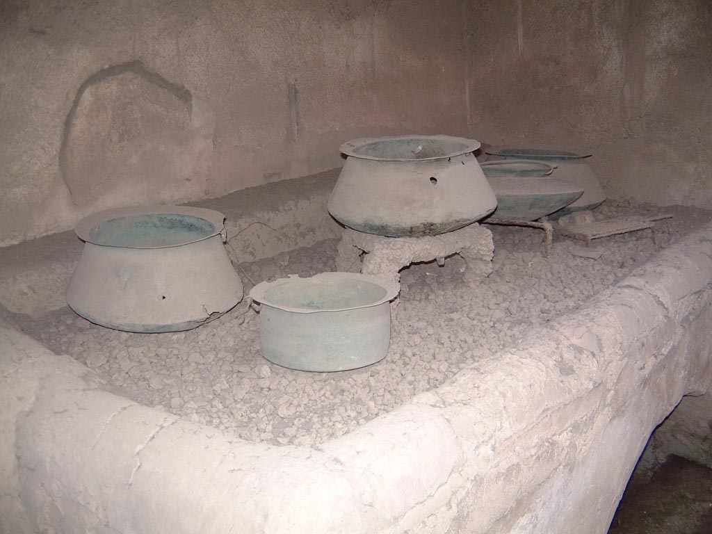 VI.15.1 Pompeii. Undated old photograph. Kitchen oven in service area with pot on tripod on embers and storage pots on floor.