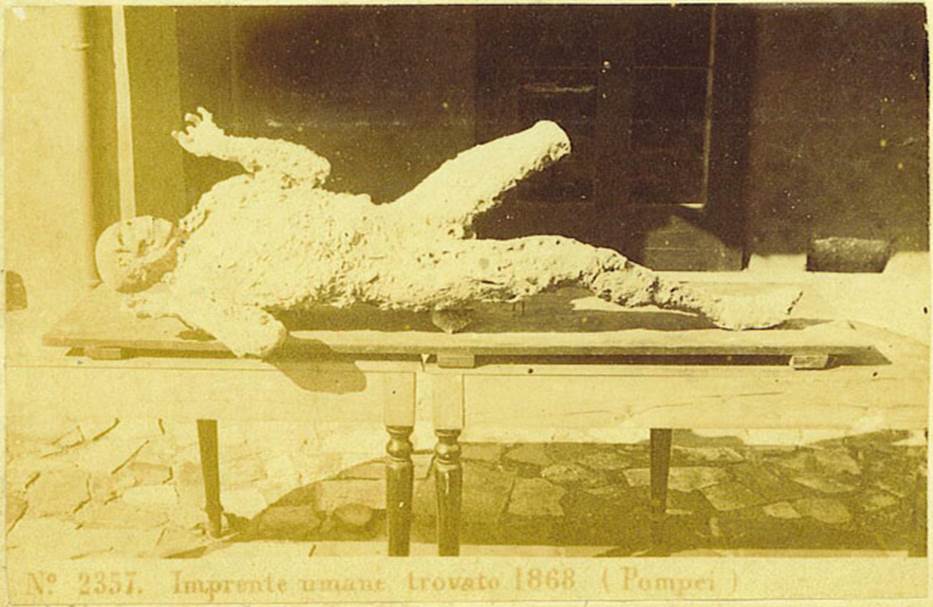 VII.2.16 Pompeii. One of the seven skeletons found in the house on 12th March 1868. Photo courtesy of Rick Bauer. Seven skeletons were found, but six of them had not left enough imprint in the cinders to make a good plaster cast. The above was the only successful one, although his left leg was not cast, on his face was a look of horror.
See Garcia y Garcia, L., 2006. Danni di guerra a Pompei. Rome: LErma di Bretschneider. (p.190)
According to Dwyer, the cast was only partially successful as the cavity had been infiltrated by lapilli and this left the skull and left leg exposed.
This cast, known as the Fifth Victim, was placed in the Archaeological School, and it was here that Ernest Breton saw it, and described
This unfortunate was discovered lying on his stomach in a room to the left of the atrium of the House of Gavius Rufus.  Six other skeletons were near him  from Breton, 1869.
See Dwyer, E., 2010. Pompeiis Living Statues. Ann Arbor: Univ of Michigan Press. (p. 80)
