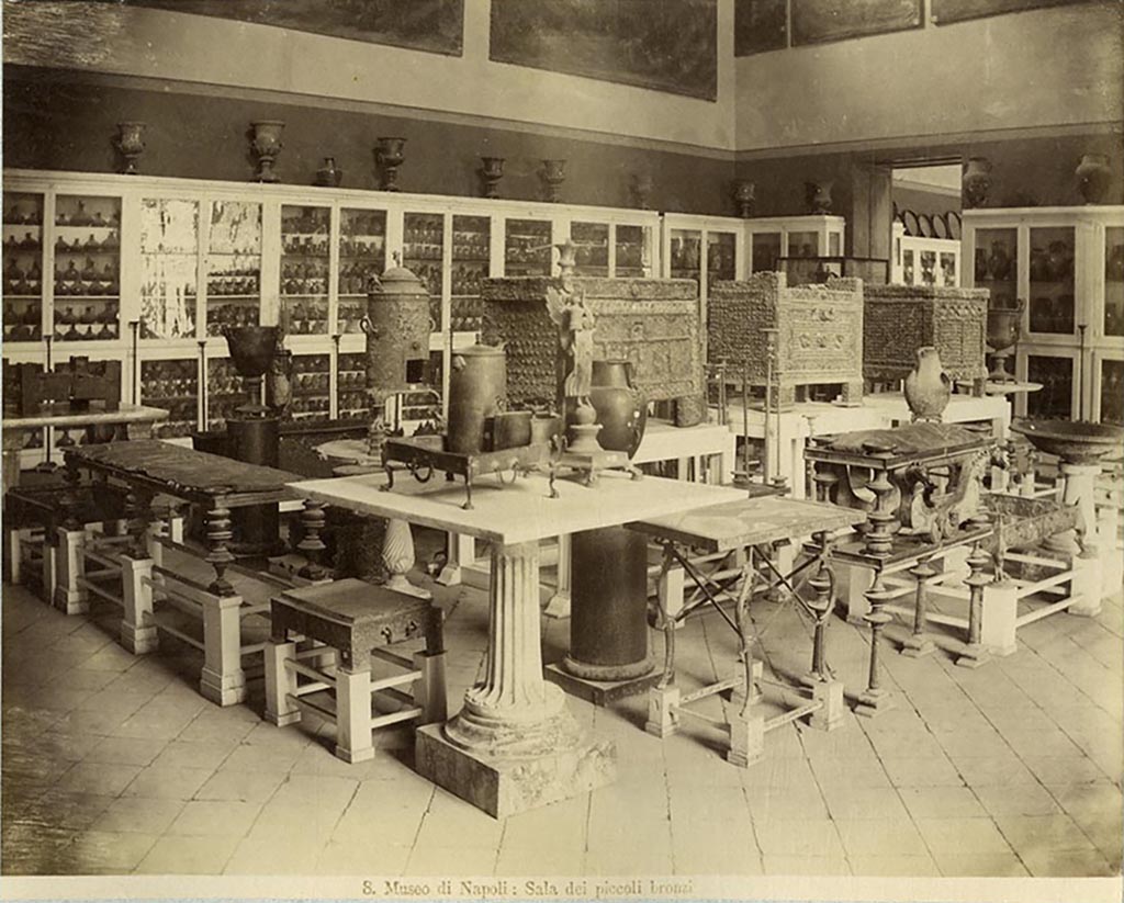 According to Milanese, in the National Archaeological Museum of Naples four arcae ferratae (money chests) are preserved: 
Three safes are documented in the above photo [left to right], from around 1885, from the Sala dei Piccoli Bronzes made by the photographer Achille Mauri.
The safe with sacrifice to Jupiter [from VII.7.5], inv. 73020.
The safe [from VII.2.18] with Eros and Psyche, inv. 73021. 
The safe with busts of deities [from Pompeii], inv. 73022.
The fourth safe from the House of the Vettii restored by the Central Institute for the Restoration was not discovered until after this photograph was taken. 
See Milanese, A., 2009. Album museo. Immagini fotografiche ottocentesche del Museo Nazionale di Napoli, Napoli, pp. 156-161.
