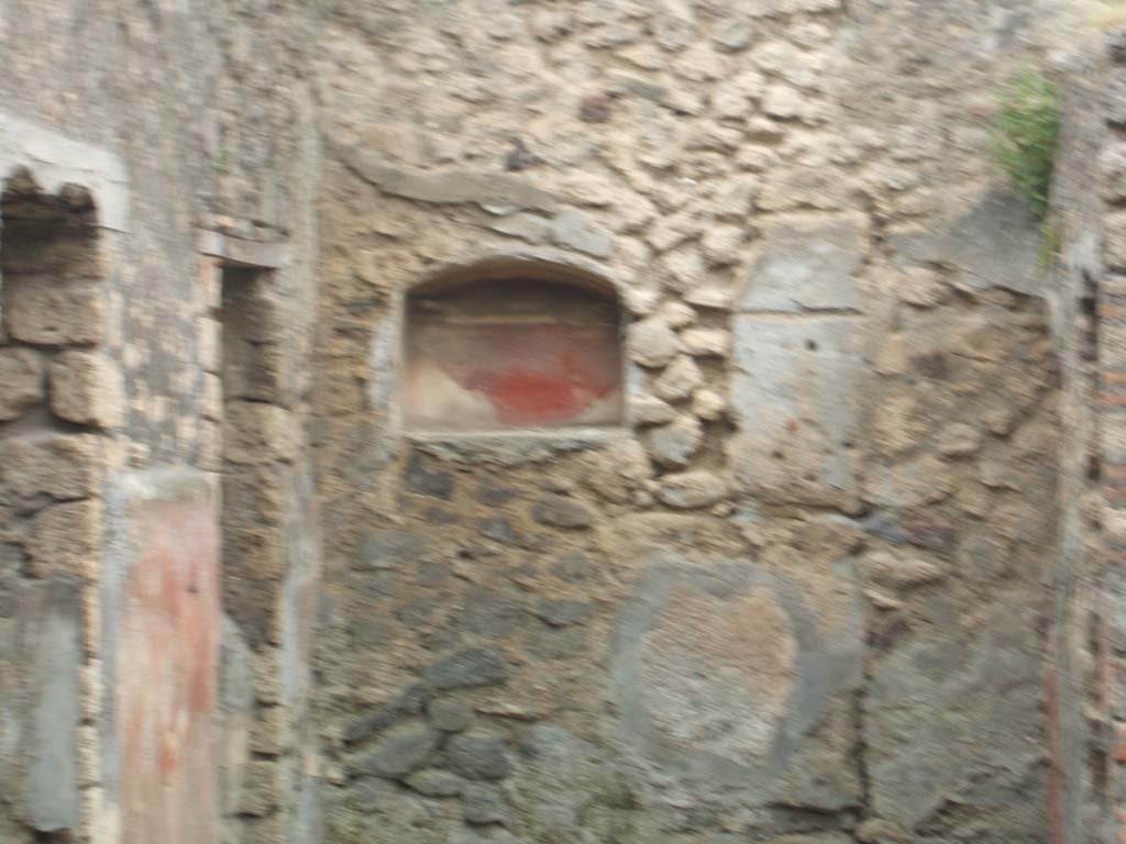 IX.9.13 Pompeii. May 2005. Room 6, arched niche set in west wall in south-west corner of garden. 
According to Boyce –
On the wall to the right of the niche was the lararium painting: on the left stands a tripod of unusual form with a dark coloured vessel upon it. The Genius, standing to the right, pours a libation upon the tripod; he wears a wreath of leaves; the toga does not seem to be drawn over hs head as usual, though the preservation of the painting is poor at this point; he holds no cornucopia. Behind and to the right stand two figures: in the first plane, a camillus, also wreathed, and carrying fruit in a shallow dish; above and farther right, a popa, wreathed and carrying an axe.
To the left of the Genius are two wreathed figures apparently women, though it is impossible to be certain, for only the upper portions of their figures are preserved. 
On the left side of the niche there was not room for painted figures, but on the adjoining south wall the figure of the Genius appears again, clad in white toga and pouring a libation upon a yellow cylindrical altar with a fire; he is unbearded, his flesh is reddish, and in is left hand he holds a yellow cornucopia.
This double Genius certainly has some special significance. …….
See Boyce G. K., 1937. Corpus of the Lararia of Pompeii. Rome: MAAR 14. (p. 93, no. 466).
See Notizie degli Scavi di Antichità, 1891, p. 258
See Jashemski, W. F., 1993. The Gardens of Pompeii, Volume II: Appendices. New York: Caratzas. (p. 247).
