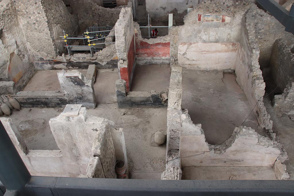 IX.12.4 Pompeii. October 2024. 
Looking east towards room “o”, upper left, room “l(L)” with red painted walls, upper centre, and room “f”, on its south side.
On the upper east wall of room “f”, the painting described as from the zoccolo of an upper room, can be seen.
Room “g” can be seen on the extreme right, with doorway into atrium “c”.  Photo courtesy of Klaus Heese.

