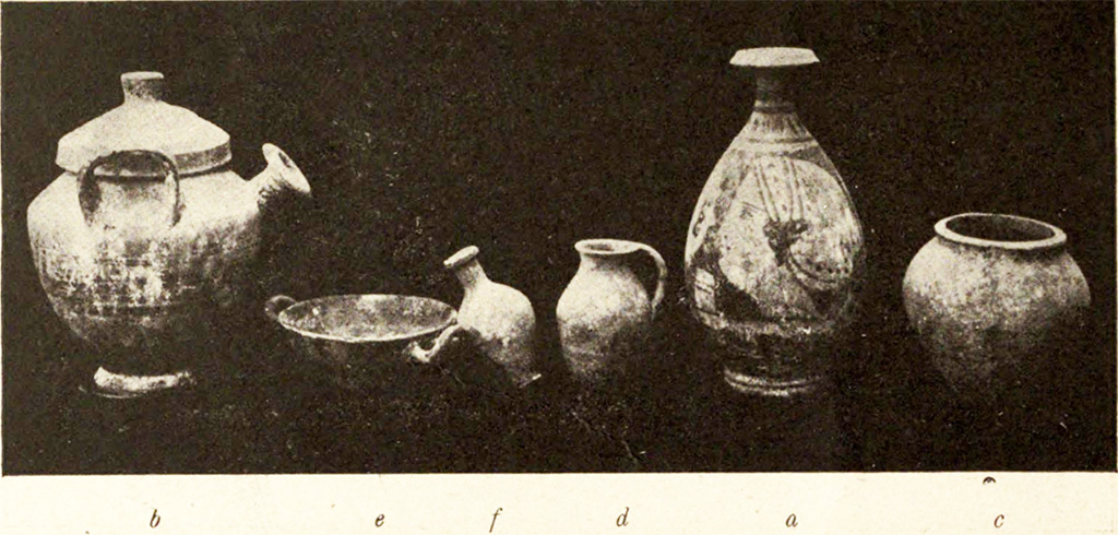 Pompeii Fondo Azzolini. Tomb VI. The photo above shows numerous objects found in the tomb.
b) Pot-bellied pitcher with vertical handles with lid (2):  height 0.20 m., and on the shoulder are the dark slats that are repeated on the lid; between the handles, from the shoulder, protrudes a cylindrical bell-shaped spout. 
e) Black-painted kylix, 0.11m in diameter, in whose bottom are the remains of a floral meander before graffiti and then painted with small white leaves.
f) Rustic ovoid jar with short neck, height 0.09 m. 
d) Rustic flask, height 0.085m., with a shapeless surplus of iron in the base. 
a) Lekythos, oval vessel, high 0.20 m, short neck: On a yellow clay background a female head in profile to the left is painted in black, while the opposite side is a palm between two whorls.
g) Iron blade, length 0.13m., broken in two pieces. 
h) Arc shaped bronze buckle, from a strap. Width 0.027m.
c) Small rustic jar in the form of a dolium, height 0.11m.  

See Notizie degli Scavi di Antichità, 1916, p. 292-3, fig. 3.
