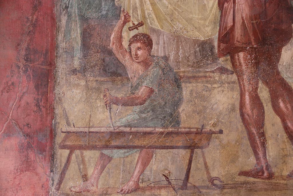 VI.15.1 Pompeii. October 2024. 
Detail from central painting showing the helper of Daedalus carrying out work with hammer and chisel. Photo courtesy of Klaus Heese.
