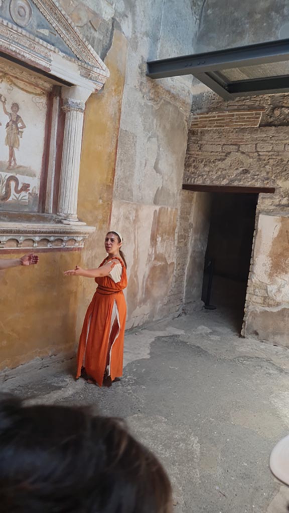 VI.15.1 Pompeii. 8th June 2024. 
Looking towards north along west side of small atrium, with doorway to kitchen (w), on left.
Historical reconstruction entitled L’altra Pompei prende vita (The other Pompeii comes to life).
